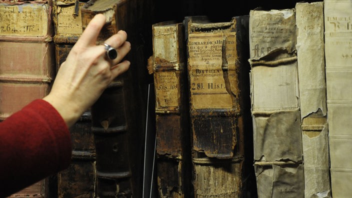 Hand greift nach einem alten Buch, das mit anderen alten Büchern im Regal steht