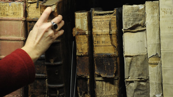 Hand greift nach einem alten Buch, das mit anderen alten Büchern im Regal steht | Bildquelle: WDR/dpa/Peter Steffen Hand greift nach einem alten Buch, das mit anderen alten Büchern im Regal steht