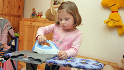 Mädchen bügelt Wäsche mit Spielzeug-Bügeleisen.