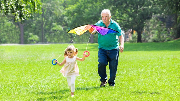Großvater hilft Enkeltochter beim Drachensteigenlassen im Park