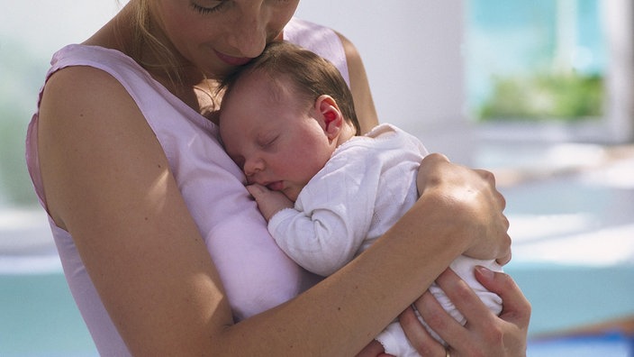 Eine junge Frau im rosa Top hält ihren schlafenden Säugling im Arm und kuschelt liebevoll mit ihm. | Bildquelle: Mauritius/Marina Raith Eine junge Frau im rosa Top hält ihren schlafenden Säugling im Arm und kuschelt liebevoll mit ihm.