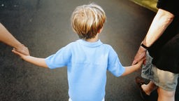 Kind hält links und rechts je eine Hand seiner Eltern.