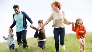 Eine Frau, ein Mann und drei Kinder rennen über eine Wiese