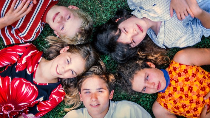 Fünf lachende Kinder liegen im Gras, ihre Köpfe berühren sich