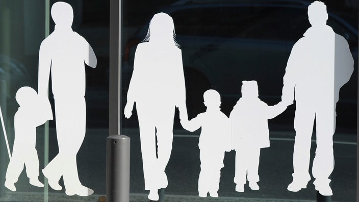Scherenschnitt-Figuren von einem Vater mit Kind und einer Familie mit Kindern auf einer Fensterscheibe