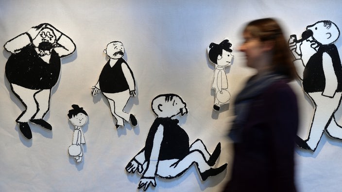 Eine Frau geht in einer Ausstellung an den Karikaturen "Vater und Sohn" vorbei