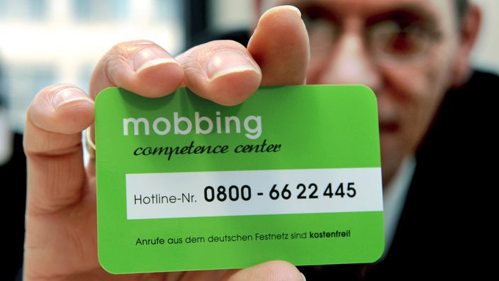 Ein Mann zeigt eine Kontakt-Karte des Mobbing Competence Centers.