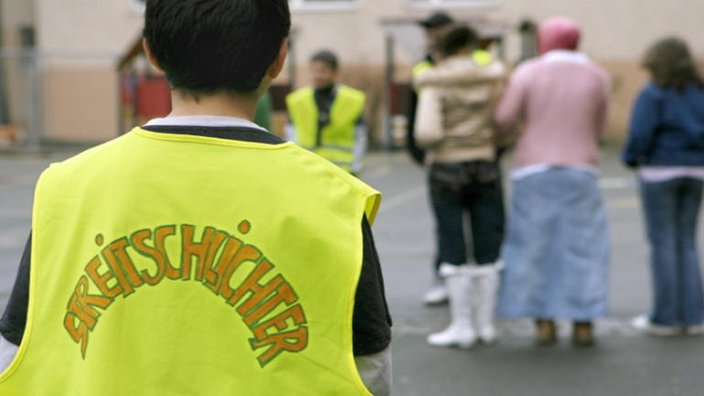 Ein Schüler in gelber Weste mit Aufschrift 'Streitschlichter' beobachtet den Schulhof während der Pause. | Bildquelle: dpa Ein Schüler in gelber Weste mit Aufschrift 'Streitschlichter' beobachtet den Schulhof während der Pause.