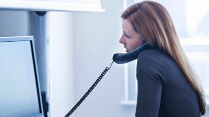 Eine Frau telefoniert im Büro vor ihren PC. 