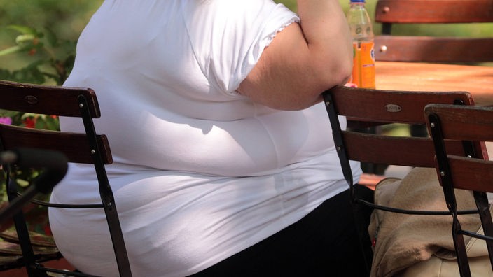 Eine extrem übergewichtige Person sitzt auf einem Gartenstuhl.