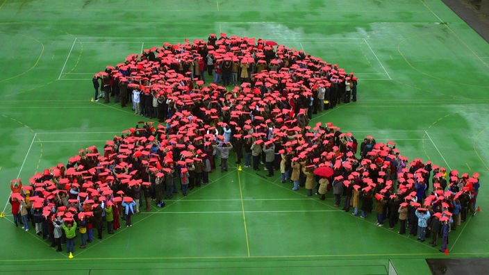 Rund 800 Schülerinnen und Schüler des Würzburger Siebold Gymnasiums stehen im Pausenhof ihrer Schule in Form einer Aidsschleife