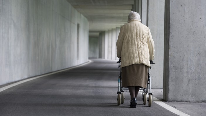 Eine alte Frau geht mit Gehhilfe spazieren.