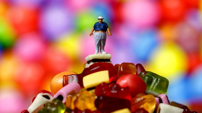 Figur eines übergewichtigen Mannes auf einem Haufen Süßigkeiten