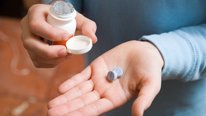 Ein Kind hält eine Medikamentendose in der einen und zwei Tabletten in der anderen Hand