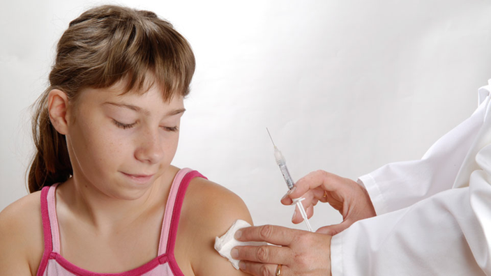 Ein besorgt auf eine Spritze blickendes Mädchen ist kurz davor, geimpft zu werden.