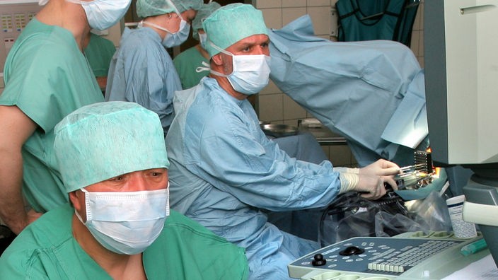 Ein Team von mehreren Ärzten mit Mundschutz und Operationskleidung bei einer Operation.