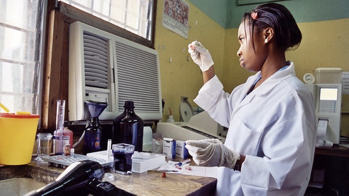 Eine Laborantin in weißem Kittel und mit weißen Handschuhen an ihrem Arbeitsplatz im Labor in Ghana.