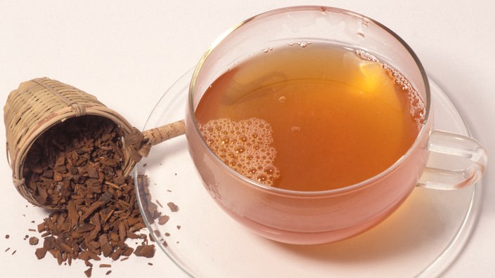 Eine Portion getrockneter Chinarinde liegt neben einer Tasse mit Tee aus Chinarinde.