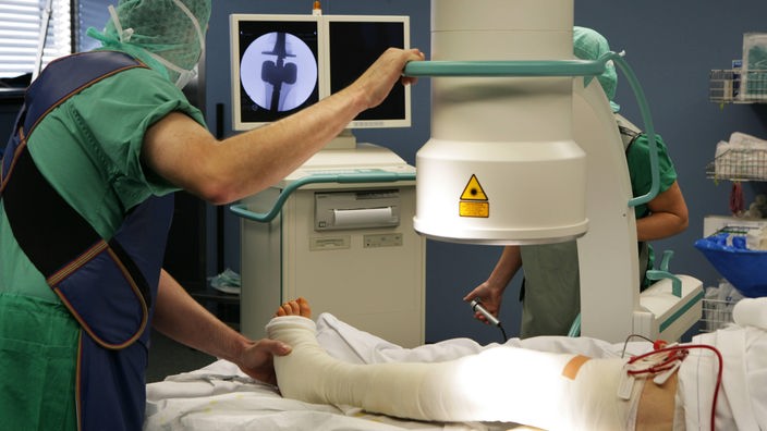 Chirurg kontrolliert ein bandagiertes Knie über ein Röntgenbild am Monitor