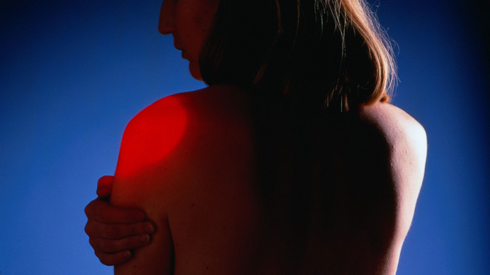 Eine junge Frau hält sich die schmerzende Schulter, rot gekennzeichnet