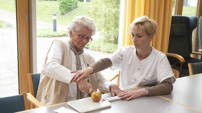 Eine Altenpflegerin betreut eine Schlaganfallpatientin bei Alltagsübungen