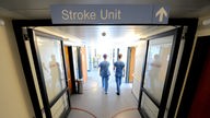 Gesundheits- und Krankenpfleger auf dem Gang einer Klinik, darüber ein Schild "Stroke Unit"