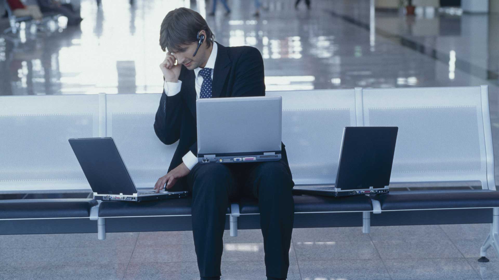 Mann arbeitet mit drei Laptops und Headset am Flughafen.