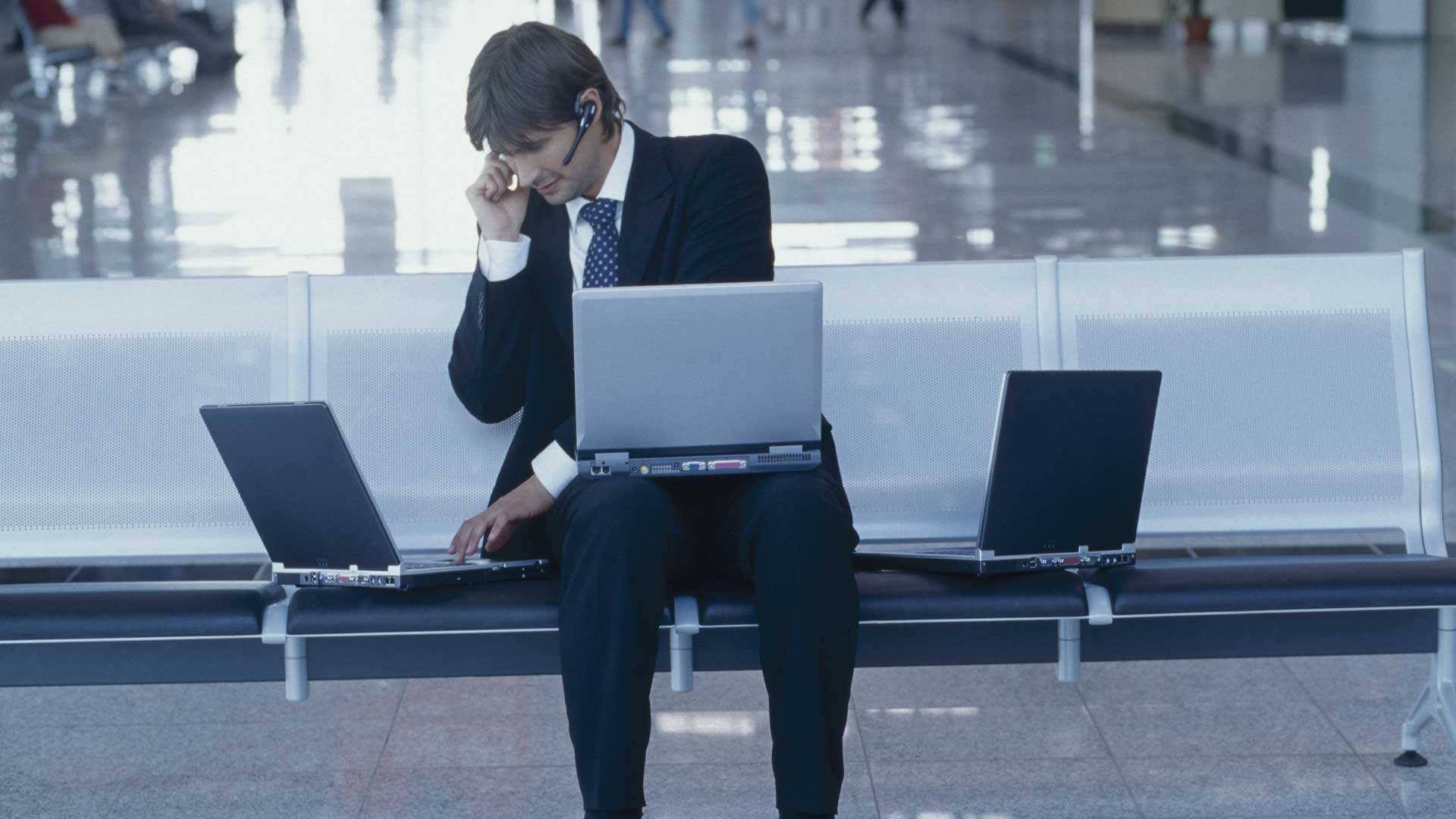 Mann arbeitet mit drei Laptops und Headset am Flughafen. | Bildquelle: WDR / mauritius images Mann arbeitet mit drei Laptops und Headset am Flughafen.