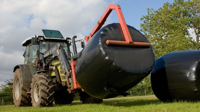 Traktor hebt einen großen Silage-Ballen an.