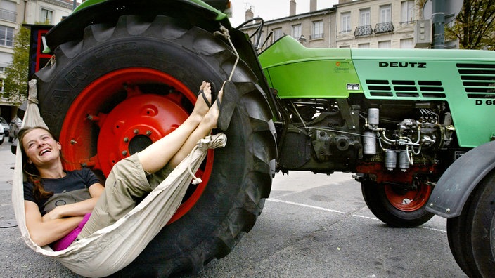 Eine Frau liegt in einer Hängematte, die an einem Traktor festgemacht ist. | Bildquelle: AFP/Philippe Merle Eine Frau liegt in einer Hängematte, die an einem Traktor festgemacht ist.
