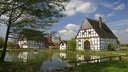 Dörfliche Idylle mit Fachwerkhäusern und einem großen Teich davor.