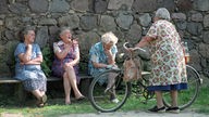 Alte Frauen sitzen auf einer Dorfbank, um Neuigkeiten auszutauschen.