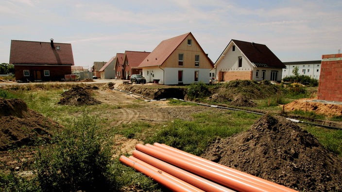 Abwasserrohre liegen auf einem Bauplatz vor bereits fertiggestellten Eigenheimen.