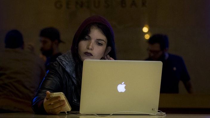 Frau in New York benutzt einen Apple Laptop. Auf der Rückseite prangt das Firmenlogo: ein angebissener Apfel.