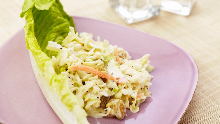 Bild von einem Krautsalat in einem Salatblatt auf einem rosa Teller. | Bildquelle: mauritius images/foodcollection Bild von einem Krautsalat in einem Salatblatt auf einem rosa Teller.