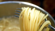 Spaghetti werden mit Gabel aus Kochtopf geholt