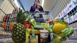 Eine Frau schiebt ihren gefüllten Einkaufswagen durch einen Supermarkt.