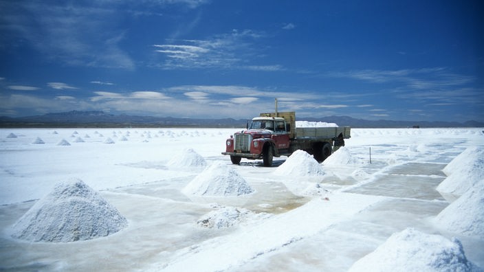 Ein Photo von einem Laster, der auf dem Salzsee vor einem kleinerem Haufen Salz steht.