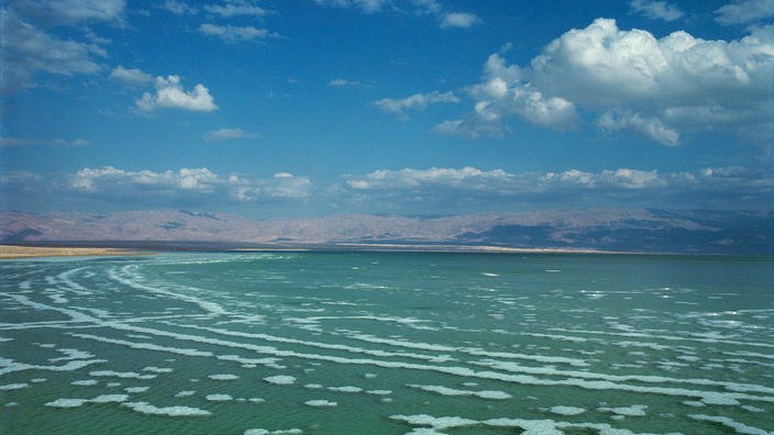 Salzschollen im Toten Meer sind als weiße Flecken im blauen Meer zu erkennen.