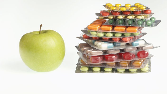 Neben einem Apfel liegt ein Stapel Tablettenpackungen
