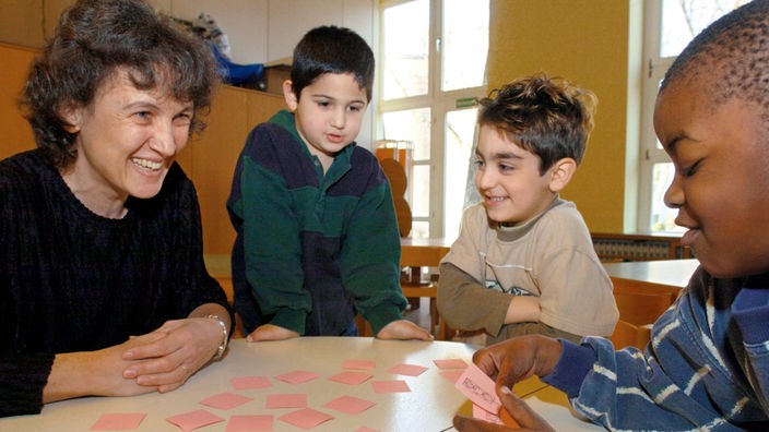 Drei Kinder lernen unter Anleitung einer Erzieherin im Kindergarten Buchstaben