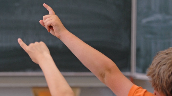 Schulkinder sitzen im Klassenraum und zeigen auf