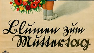 Auf einem Plakat steht in Sütterlin geschrieben: "Blumen zum Muttertag".