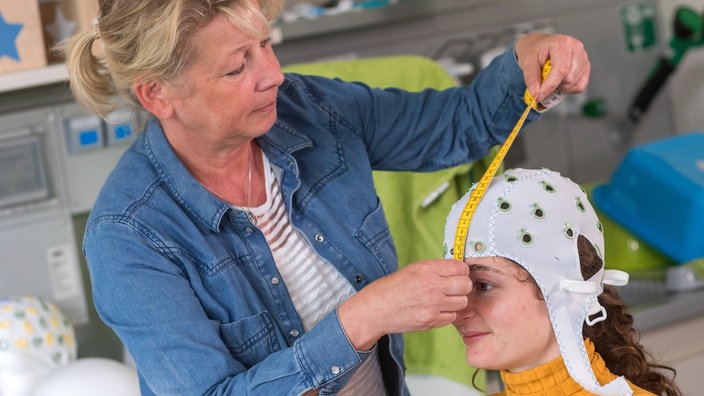 Eine Frau bereitet eine Probandin für ein Elektroenzephalogramm vor | Bildquelle: dpa/Jens Büttner Eine Frau bereitet eine Probandin für ein Elektroenzephalogramm vor