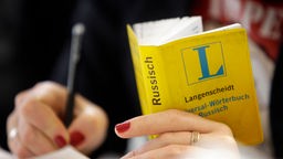 Eine Frau hält ein Russisch-Wörterbuch in der Hand und schreibt auf einem Blatt Papier