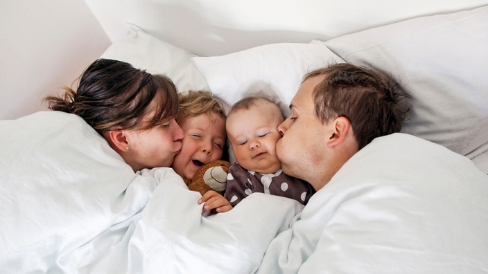 Eine Familie liegt im Bett. | Bildquelle: picture alliance / phototek / Thomas Trutschel Eine Familie liegt im Bett.