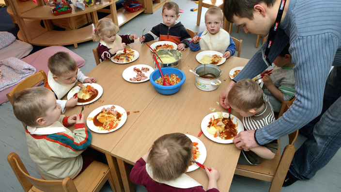 Ein Erzieher kümmert sich um Kinder, die gerade Mittag essen | Bildquelle: dpa Ein Erzieher kümmert sich um Kinder, die gerade Mittag essen