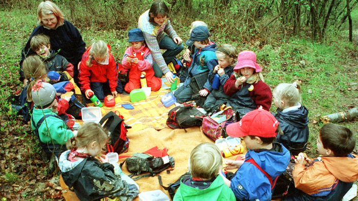 Kinder des Natur- und Waldkindergarten Erfurt frühstücken mit zwei Erzieherinnen im Stadtwald