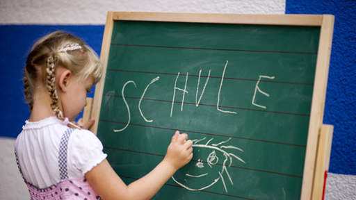 Ein kleines Mädchen schreibt auf eine Tafel.