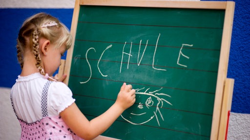 Ein kleines Mädchen schreibt auf eine Tafel. | Bildquelle: dpa Ein kleines Mädchen schreibt auf eine Tafel.